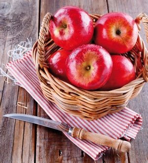 Red organic apples in a straw basket on wooden background Jabolka